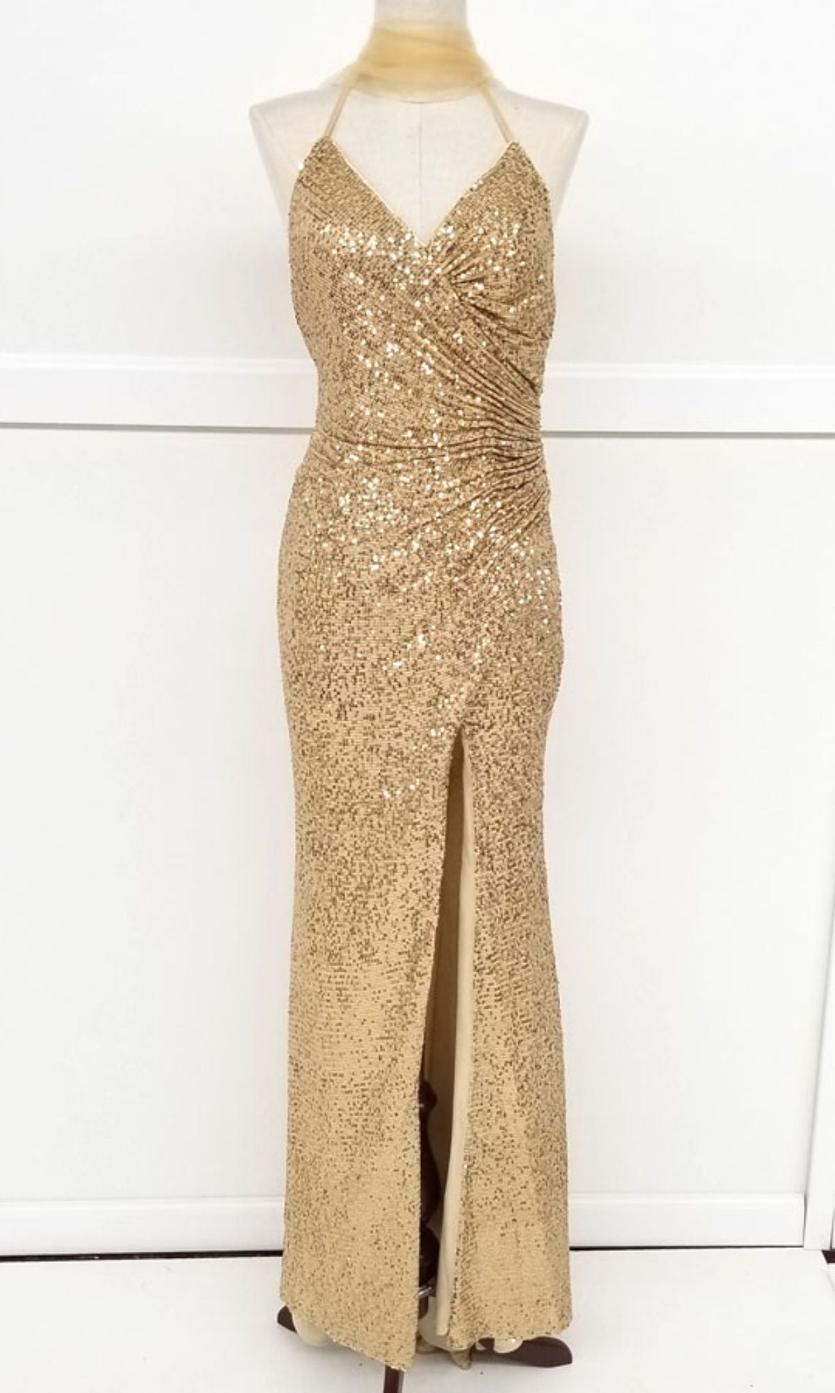 The Lace-Up Long Sequin Prom Dress: Chicas C2402 features a halter neck, ruched bodice, and front slit, sparkling with gold sequins. Shown on a dress form against a white background.